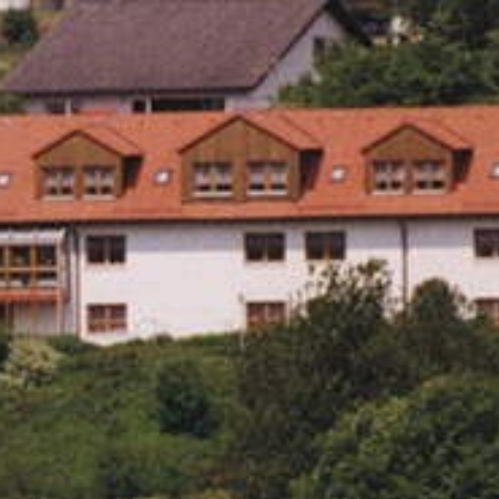 Ein älterer Mann wird von einer Pflegekraft bei Dehnübungen in Innenräumen unterstützt.